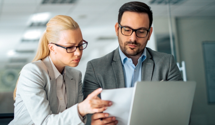 two people with glasses viewing paper in front of laptop