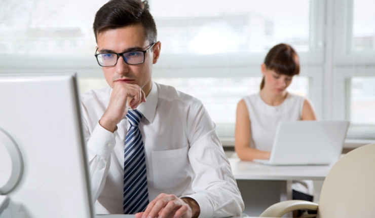 two people at respective desks, one viewing laptop, one using laptop